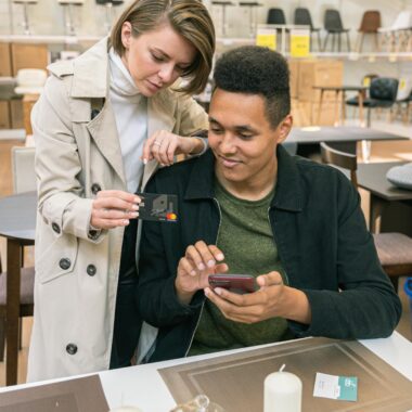 A couple makes a credit card payment using a smartphone in a modern furniture store.