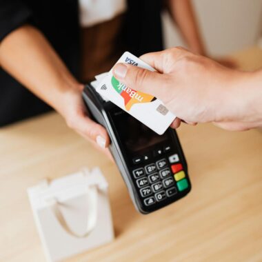 A person using a credit card for contactless payment at a retail counter.